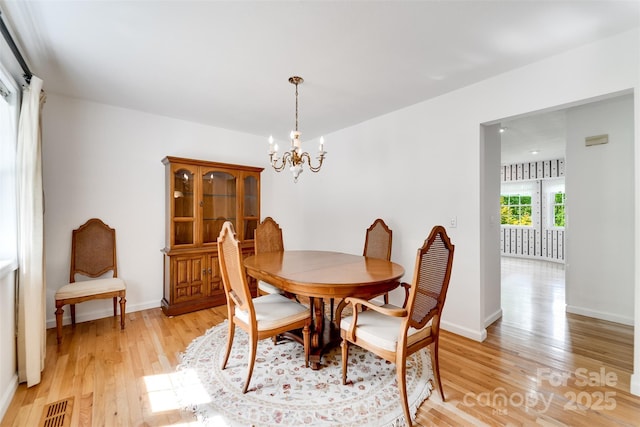dining room with baseboards, visible vents, light wood-style floors, and a notable chandelier