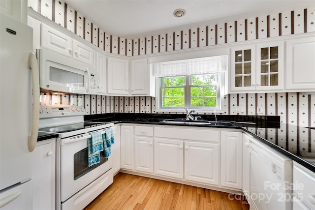 kitchen with dark countertops, white appliances, a sink, and white cabinetry