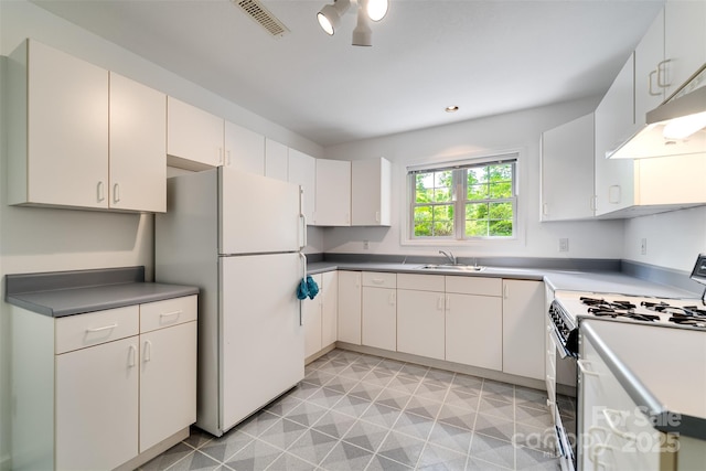 kitchen featuring a sink, visible vents, freestanding refrigerator, range with gas stovetop, and under cabinet range hood