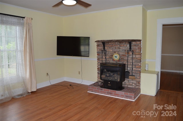 unfurnished living room featuring hardwood / wood-style flooring, a wood stove, ceiling fan, and crown molding