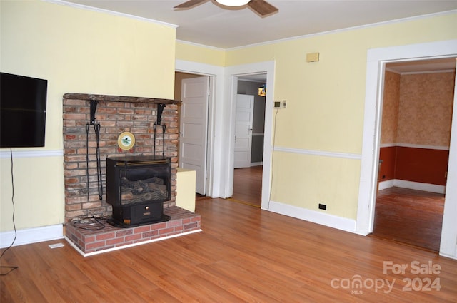 unfurnished living room featuring hardwood / wood-style floors, ceiling fan, ornamental molding, and a wood stove