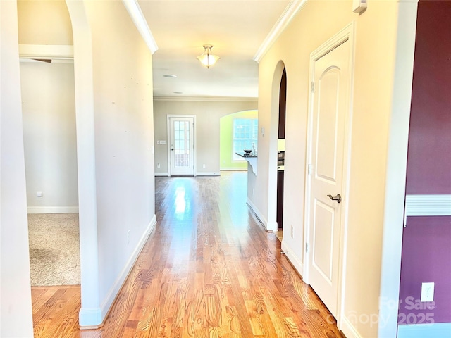 hall with ornamental molding, arched walkways, and light wood-style flooring