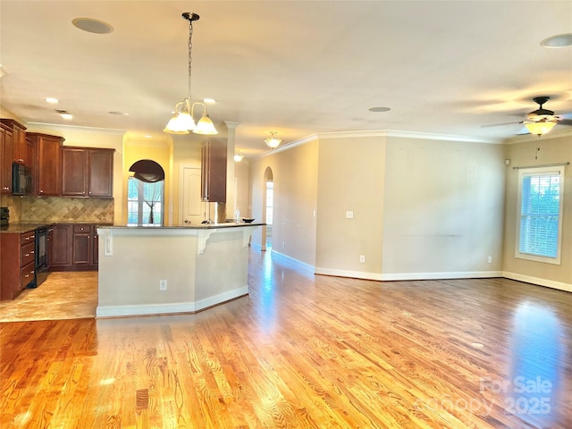 kitchen featuring dark countertops, light wood-style flooring, open floor plan, a kitchen breakfast bar, and black appliances