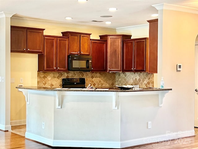 kitchen with a peninsula, black microwave, a kitchen breakfast bar, and range with electric stovetop