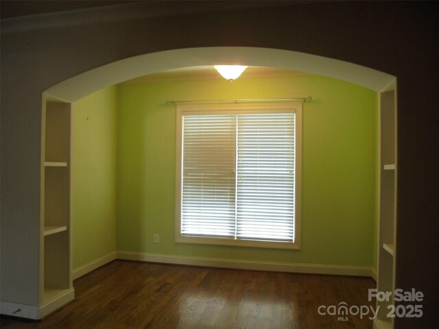 interior space with dark wood-type flooring, arched walkways, and baseboards