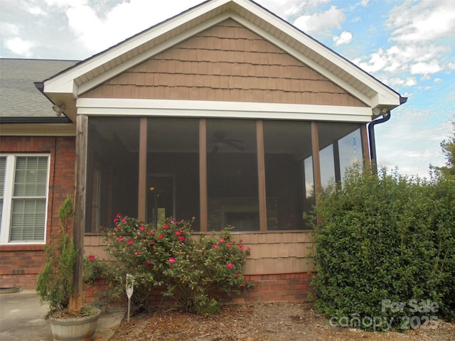 view of side of property with a sunroom, a shingled roof, and brick siding