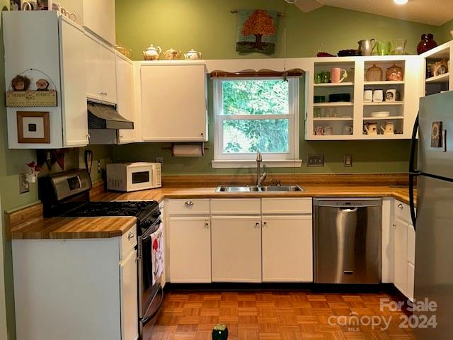 kitchen with stainless steel appliances, vaulted ceiling, sink, white cabinets, and light parquet flooring