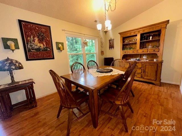 dining area featuring a notable chandelier, wood-type flooring, and vaulted ceiling