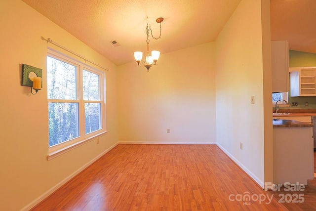 spare room featuring a sink, visible vents, baseboards, light wood finished floors, and an inviting chandelier