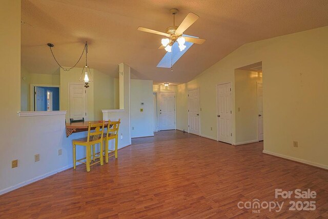 unfurnished living room with baseboards, vaulted ceiling with skylight, a ceiling fan, and wood finished floors