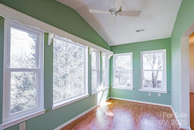 spare room featuring lofted ceiling, a textured ceiling, visible vents, baseboards, and light wood-type flooring