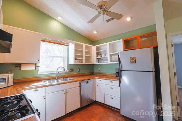 kitchen with lofted ceiling, appliances with stainless steel finishes, a textured ceiling, white cabinetry, and a sink