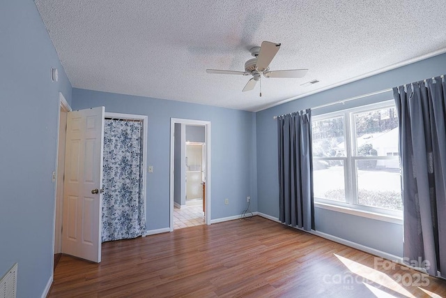 unfurnished bedroom with visible vents, a ceiling fan, a textured ceiling, wood finished floors, and baseboards