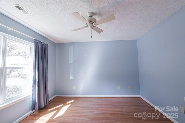 empty room featuring baseboards, a textured ceiling, visible vents, and light wood-style floors