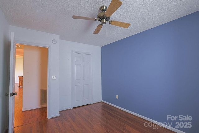 unfurnished bedroom featuring a textured ceiling, wood finished floors, visible vents, baseboards, and a closet