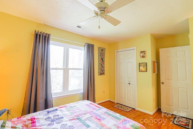 bedroom featuring light wood finished floors, visible vents, baseboards, ceiling fan, and a textured ceiling