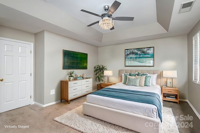 carpeted bedroom with a raised ceiling and ceiling fan