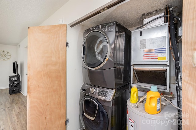 laundry area featuring stacked washer / dryer, light hardwood / wood-style flooring, and a textured ceiling