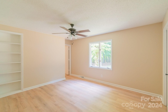 unfurnished room featuring a textured ceiling, ceiling fan, light hardwood / wood-style floors, and built in shelves