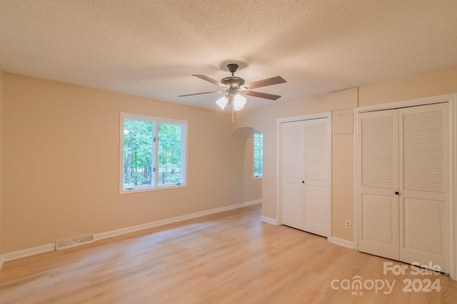 unfurnished bedroom featuring ceiling fan, multiple closets, a textured ceiling, and light hardwood / wood-style flooring