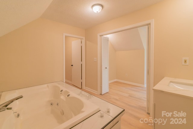 bathroom with vanity, vaulted ceiling, a tub, wood-type flooring, and a textured ceiling