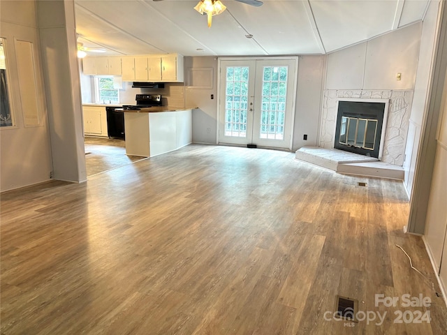 unfurnished living room featuring a stone fireplace, ceiling fan, light hardwood / wood-style flooring, and french doors