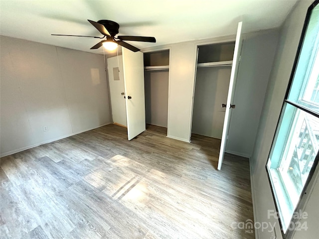 unfurnished bedroom featuring ceiling fan, light hardwood / wood-style flooring, and two closets