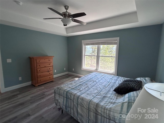 bedroom featuring a raised ceiling, ceiling fan, and dark hardwood / wood-style floors