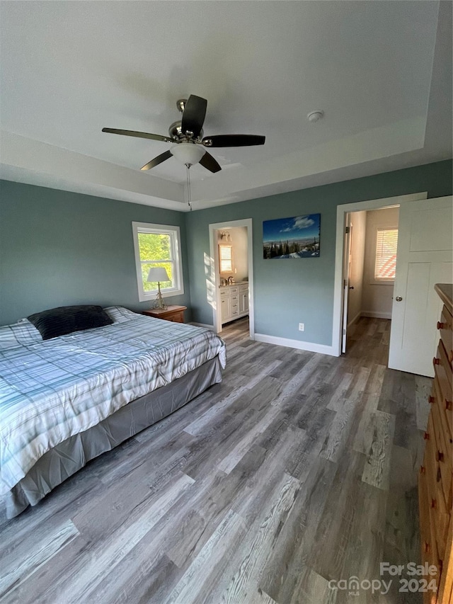 unfurnished bedroom featuring ceiling fan, wood-type flooring, a tray ceiling, and ensuite bath