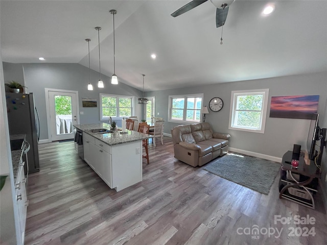 kitchen featuring light stone countertops, white cabinets, stainless steel appliances, hanging light fixtures, and a center island with sink