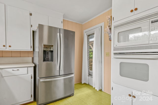 kitchen with wood walls, stainless steel fridge, white microwave, crown molding, and white cabinets