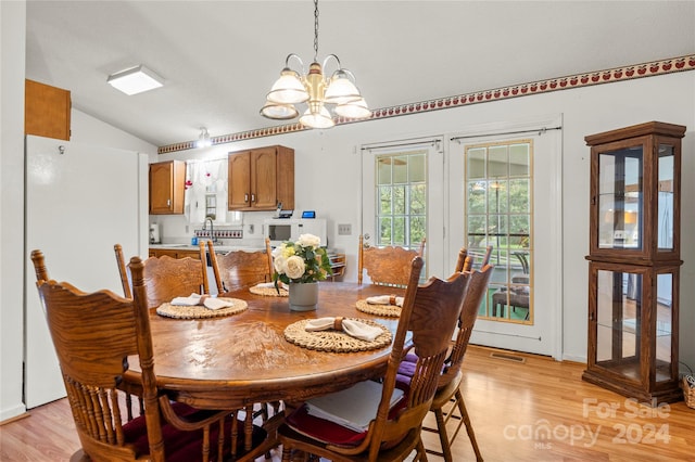 dining room with a notable chandelier, light wood-type flooring, and vaulted ceiling