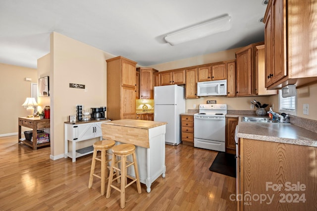 kitchen featuring white appliances, a kitchen bar, sink, and light hardwood / wood-style floors