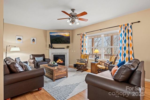 living room featuring a fireplace, ceiling fan, and light wood-type flooring