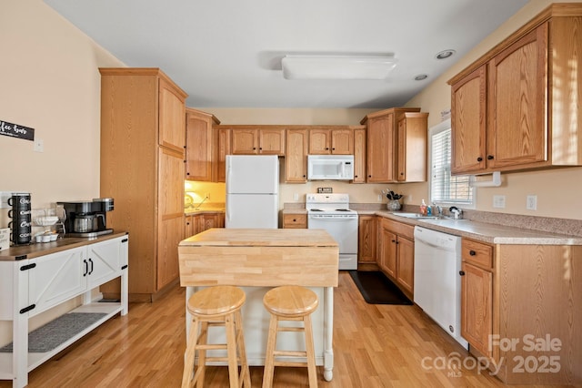 kitchen with white appliances, a kitchen breakfast bar, sink, and light wood-type flooring