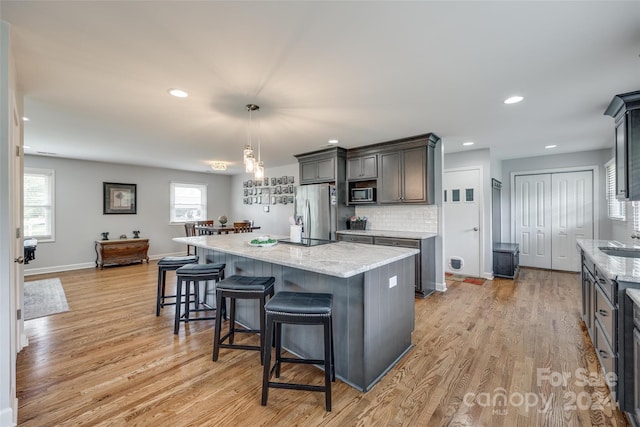 kitchen with stainless steel fridge with ice dispenser, light hardwood / wood-style flooring, backsplash, decorative light fixtures, and a kitchen island