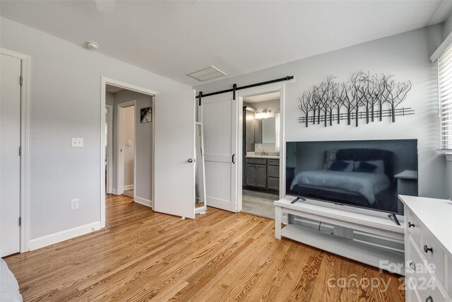 bedroom featuring a barn door, light hardwood / wood-style floors, and connected bathroom