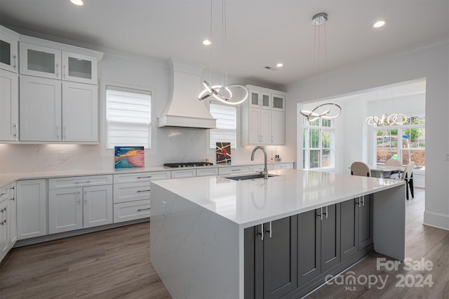 kitchen with a kitchen island with sink, backsplash, custom exhaust hood, sink, and dark wood-type flooring