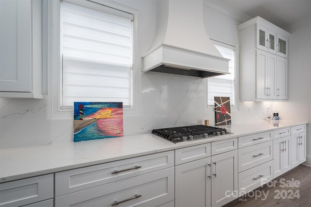 kitchen with stainless steel gas stovetop, tasteful backsplash, custom range hood, and white cabinetry