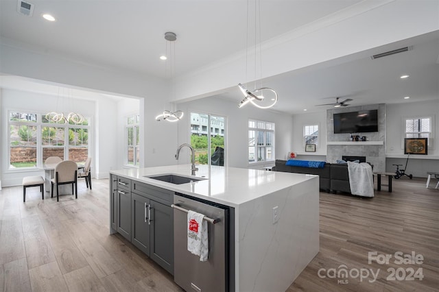 kitchen with an island with sink, dishwasher, sink, hanging light fixtures, and a tiled fireplace