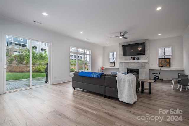 living room with a tiled fireplace, crown molding, ceiling fan, and light wood-type flooring