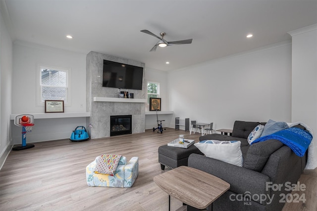 living room with a tiled fireplace, crown molding, a healthy amount of sunlight, and light wood-type flooring