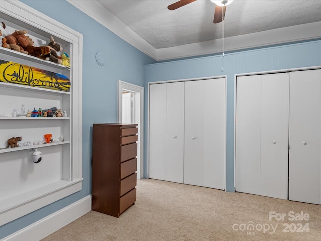 bedroom featuring ceiling fan, crown molding, a textured ceiling, light carpet, and two closets