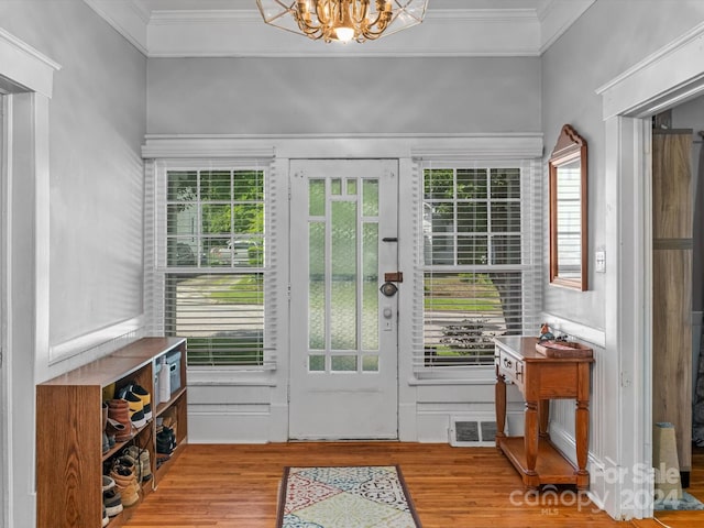 doorway featuring crown molding, light hardwood / wood-style flooring, and an inviting chandelier