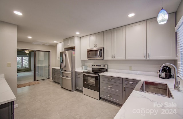 kitchen featuring appliances with stainless steel finishes, light stone counters, sink, decorative light fixtures, and gray cabinets