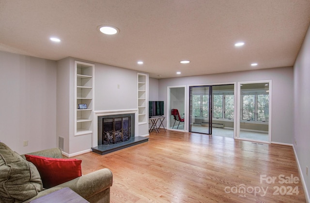 living room featuring light wood-type flooring, built in features, and a baseboard heating unit