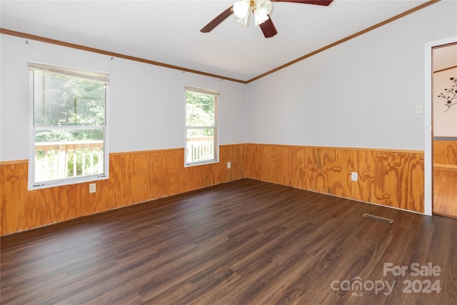 empty room featuring crown molding, ceiling fan, dark hardwood / wood-style flooring, and wood walls