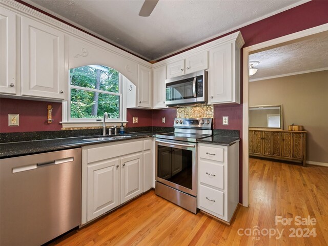 kitchen with sink, light hardwood / wood-style flooring, ornamental molding, white cabinetry, and stainless steel appliances