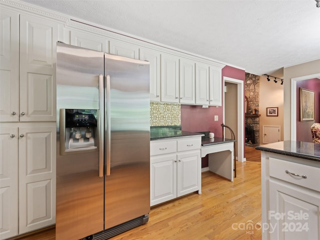 kitchen featuring backsplash, stainless steel fridge, light wood-type flooring, a fireplace, and white cabinetry