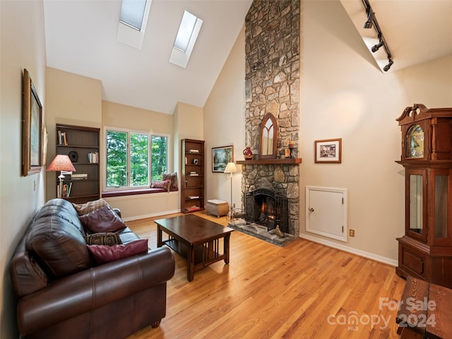 living room featuring a skylight, rail lighting, light hardwood / wood-style flooring, high vaulted ceiling, and a fireplace